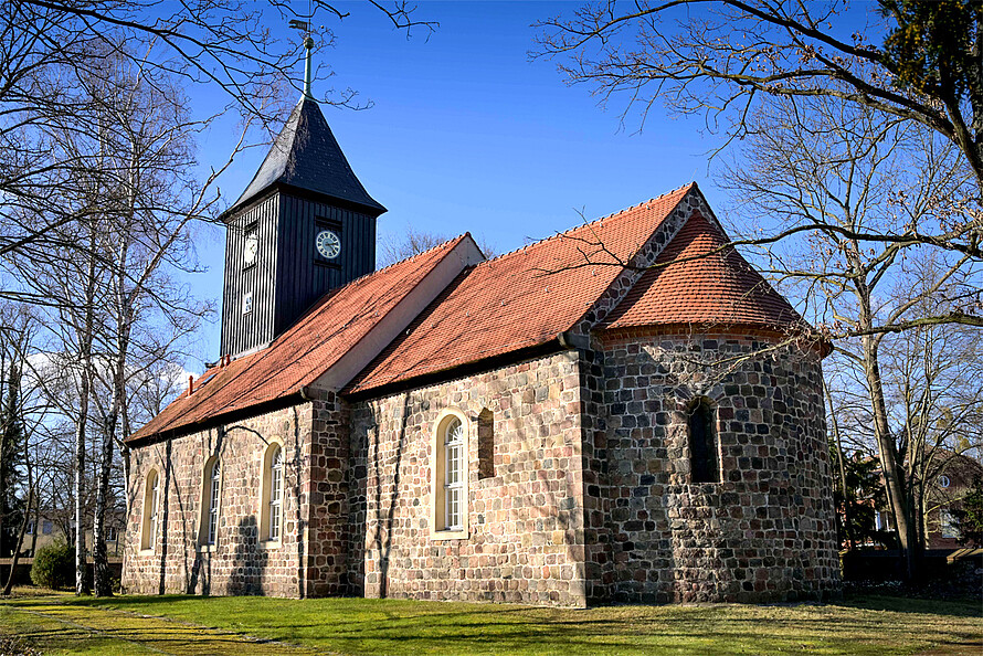 Altes Kirchengebäude aus Backsteinen mit rotem Ziegeldach und Kirchturm aus dunklem Holz.