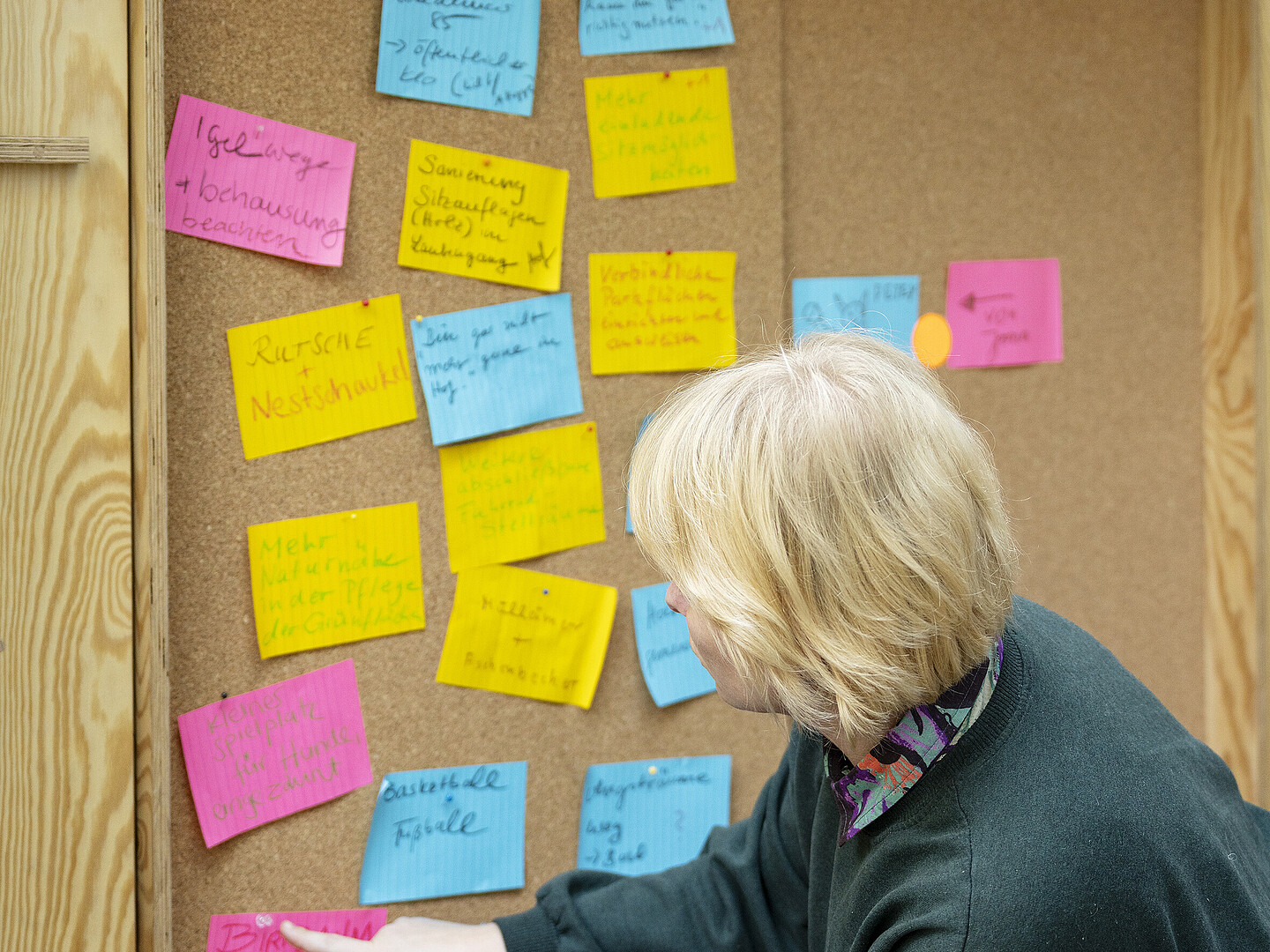 Eine Person klebt mehrere bunte Post-its an eine Korkwand.