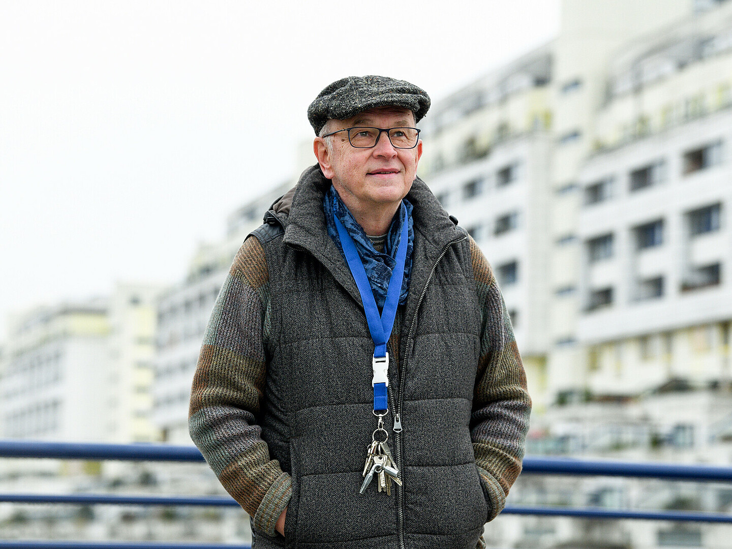 Haustechniker Dirk Schulte hat einen großen blauem Schlüsselbund um den Hals gehangen, er steht vor einem unscharfem Hintergrund, das Gebäude „Schlange“ ist erkennbar.