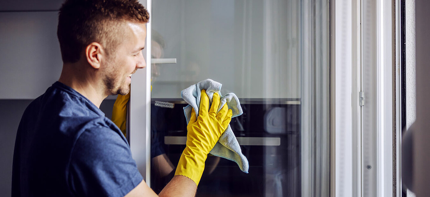 Ein Mann wischt ein Fensterglas mit einem Lappen.