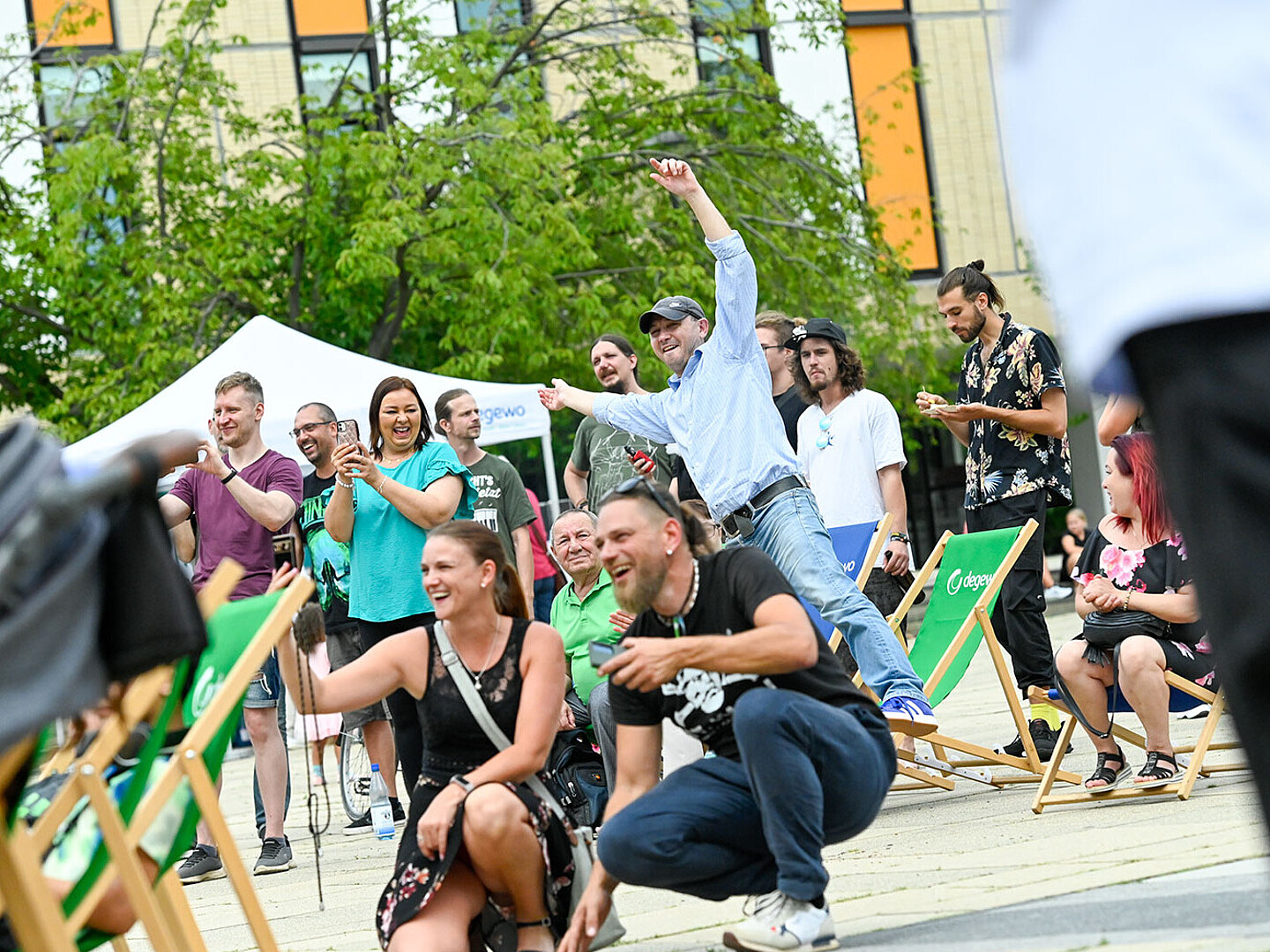 Menschen sitzen auf Stühlen vor einer Open Air Bühne und genießen das Programm. Sie tanzen und jubeln.