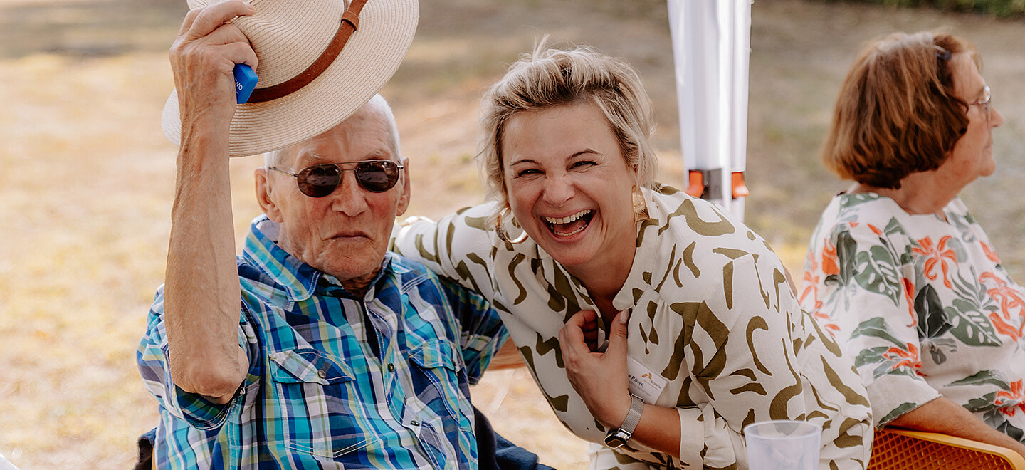Ein älterer Herr und eine Mitarbeiterin von SOPHIA lachen in die Kamera.