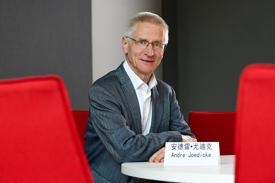 André Jödicke sitzt vor einem Schild mit seinem Namen auf Deutsch und Chinesisch.