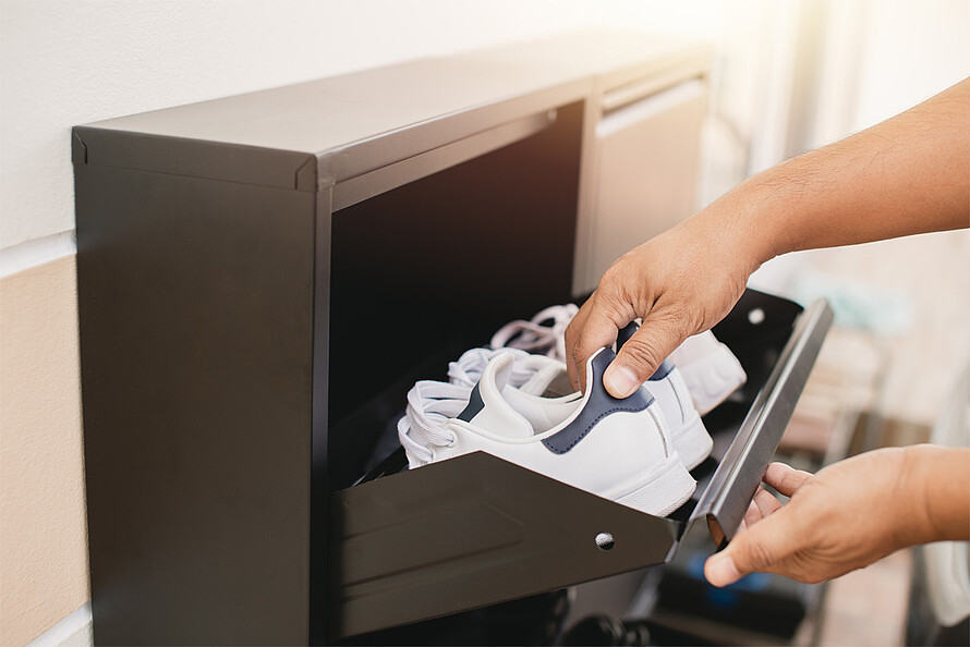 Ein Mann öffnet sein Schuhschrank und verstaut ein Paar Schuhe.