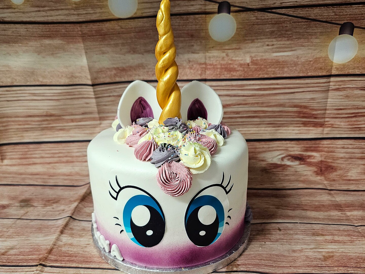 Eine Torte in Form eines Einhorns. Die Torte hat einen violett-weißen Farbverlauf, große blaue Augen und ein goldenes Horn.