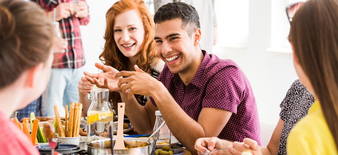 Bild zeigt lachende Menschen, die zusammen am Tisch sitzen.