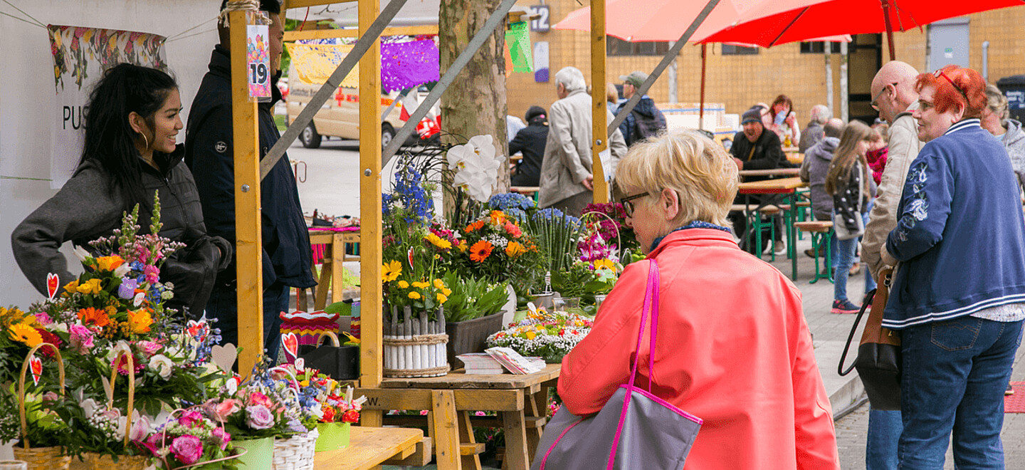 Seniorin läuft an Blumenständen vorbei.