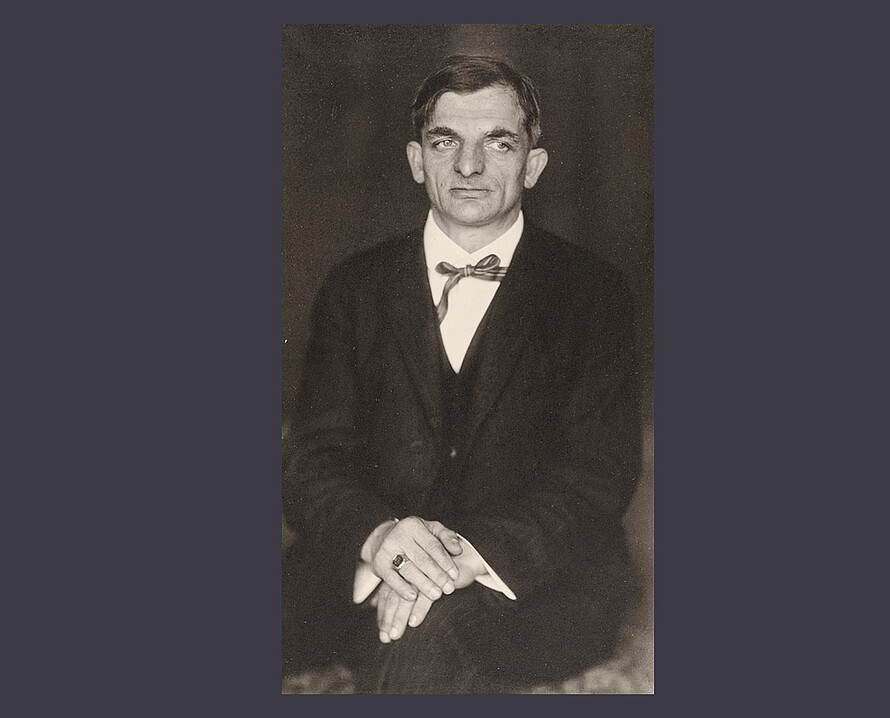 Schwarz-weiß Portraitfoto von Joachim Ringelnatz, der mit einem Anzug bekleidet ist und sitzt.