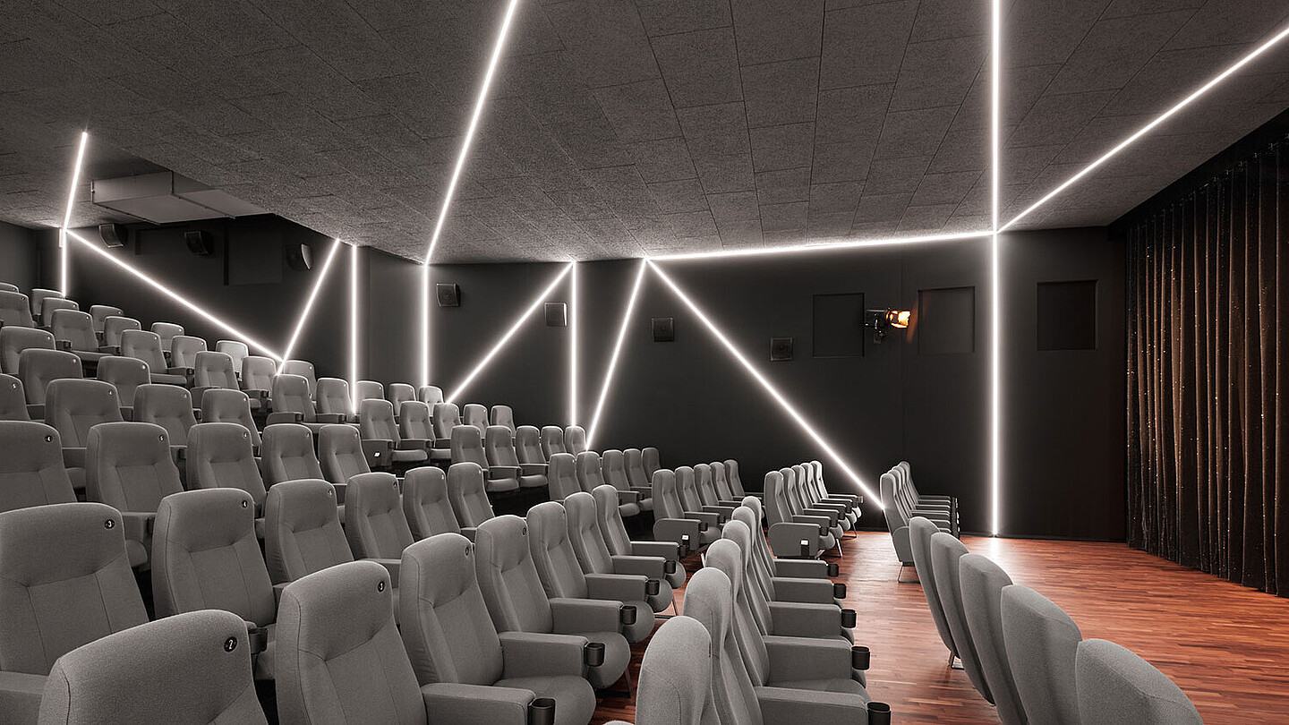 Blick in einen Kinosaal, die Leinwand ist durch einen Vorhang verdeckt. Der Raum wird durch graues Neonlicht von der Decke beleuchtet.