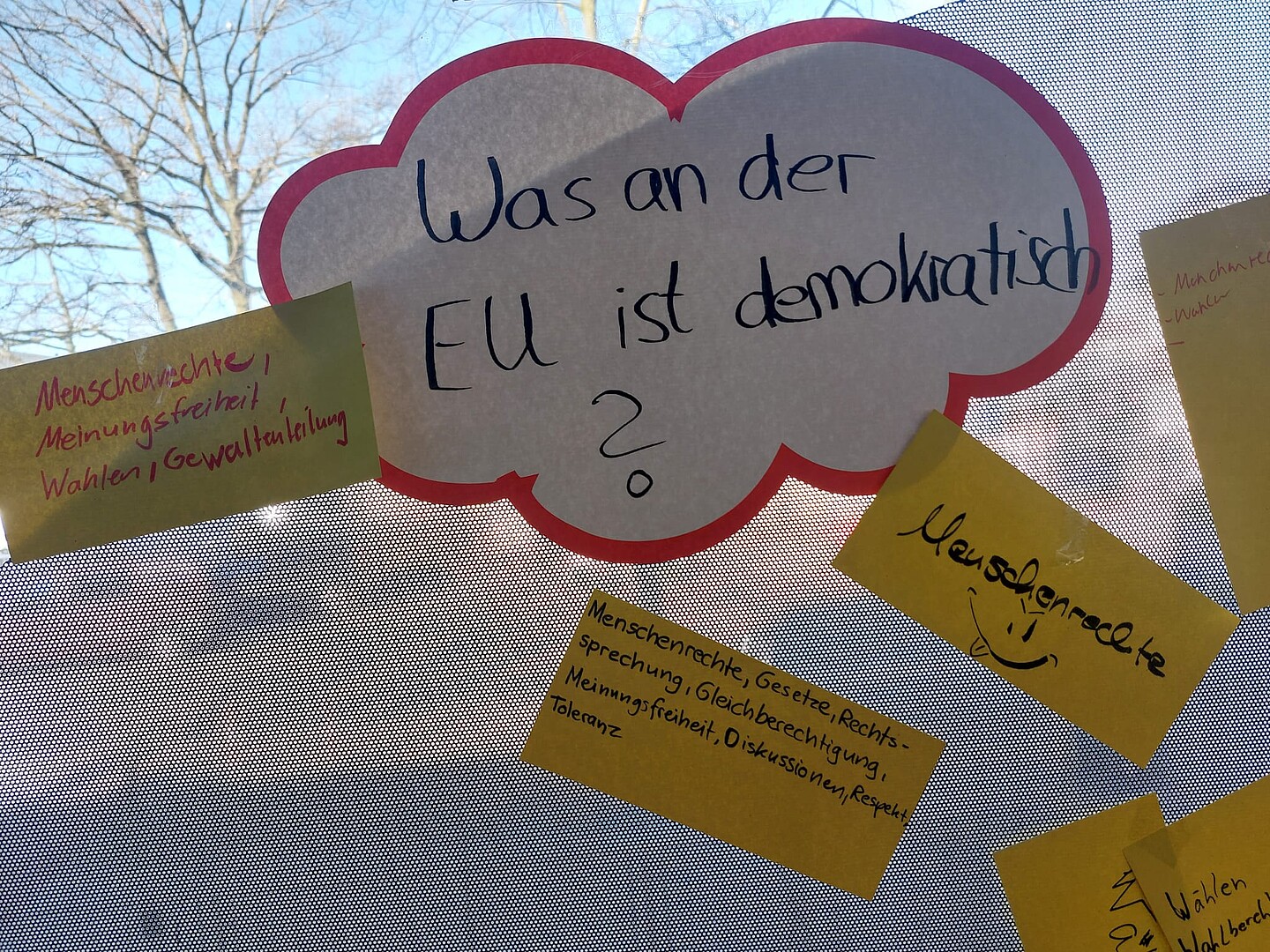 Handgeschriebene Wortwolke am Fenster mit der Frage "Was an der EU ist demokratisch?" und Notizen zu Menschenrechten, Wahlen und Meinungsfreiheit.