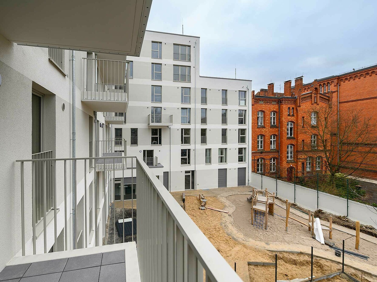 Der Blick geht von einem Balkon in den Innenhof eines Neubaus. Zu sehen ist ein Spielplatz und Sand.