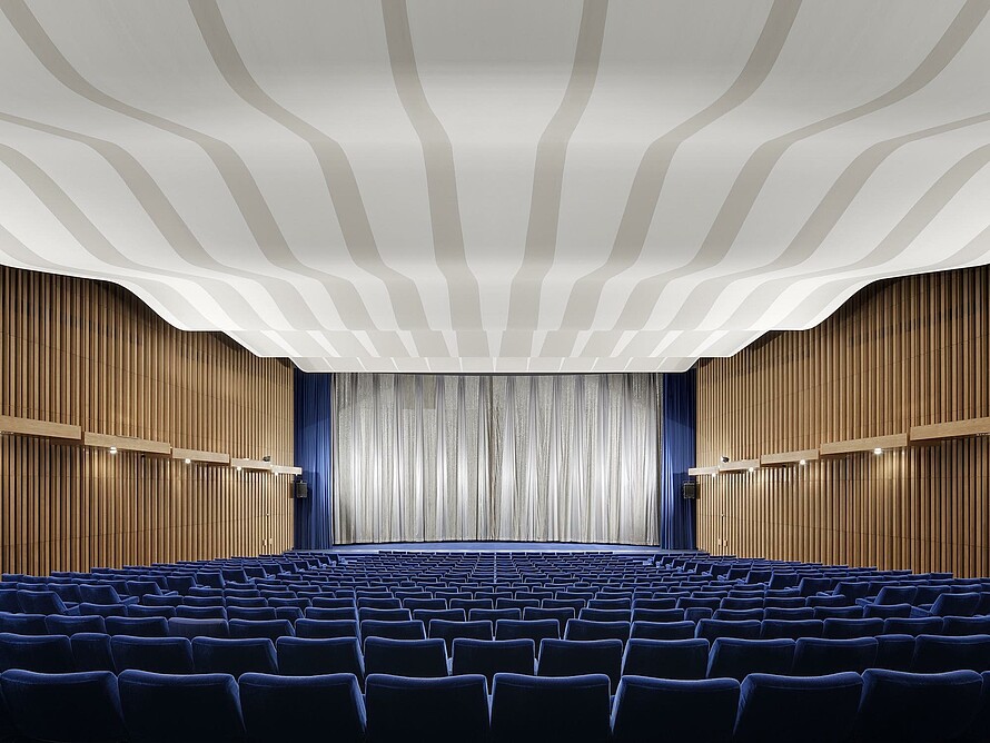 Ein Kinosaal im Kino International mit blauen Sitzreihen, holzvertäfelten Wänden und einem silbernen Vorhang vor der Leinwand 