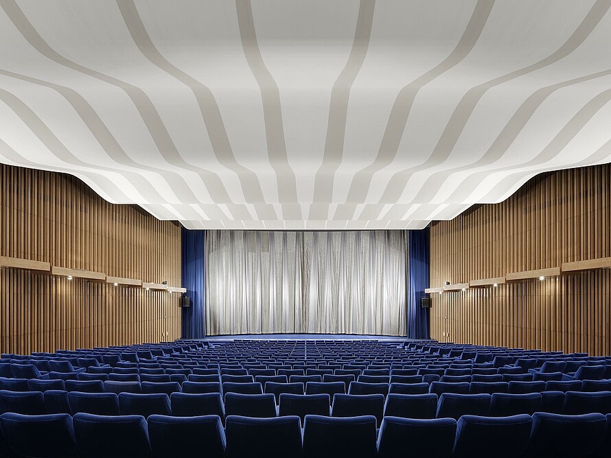 Ein Kinosaal im Kino International mit blauen Sitzreihen, holzvertäfelten Wänden und einem silbernen Vorhang vor der Leinwand