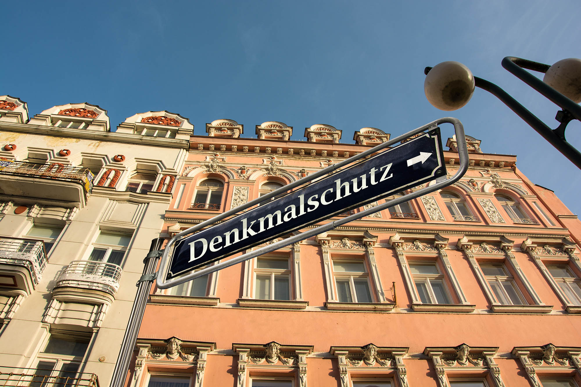 Im Hintergrund Gebäude mit Stuck und Verzierungen, im Vordergrund ein Schild mit der Aufschrift „Denkmalschutz“.