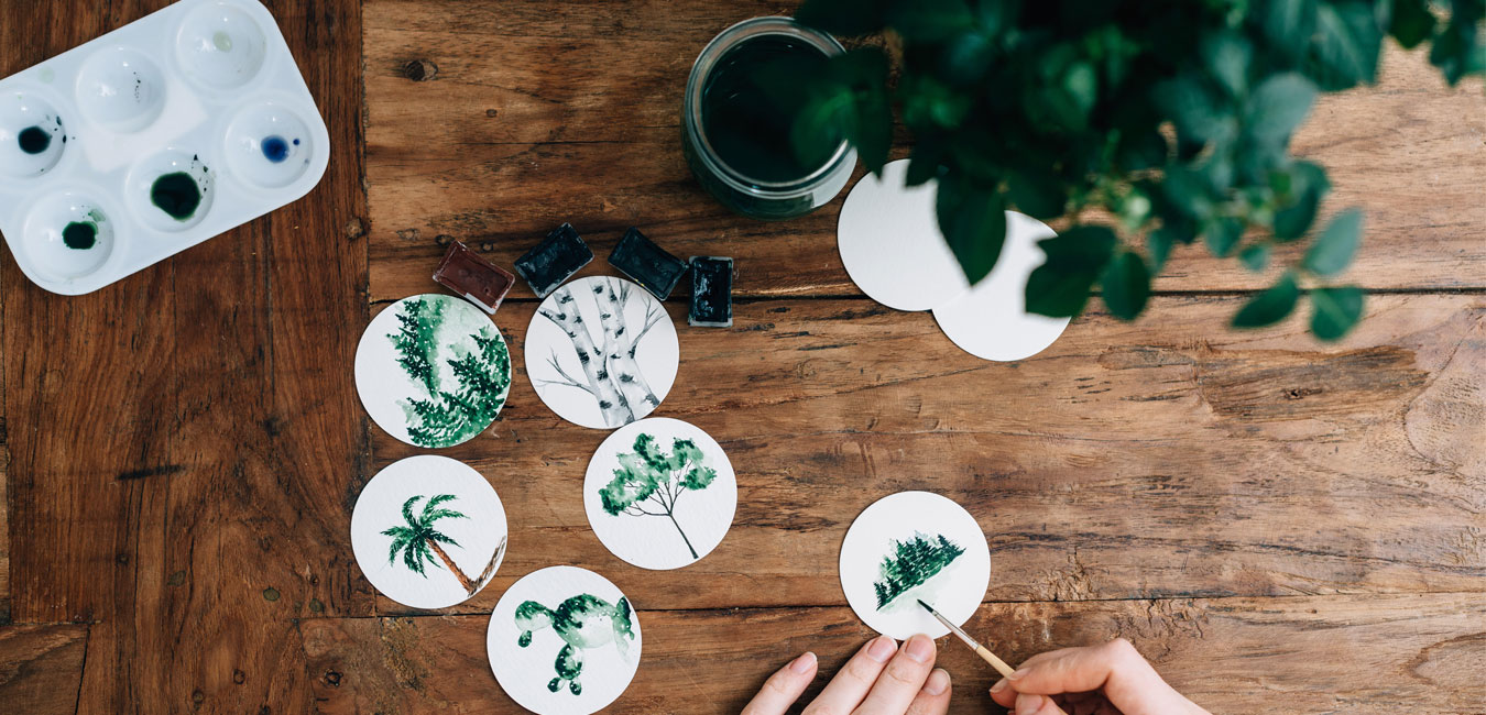 Kleine runde Bilder werden mit Wasserfarbe bemalt mit Baummotiven.