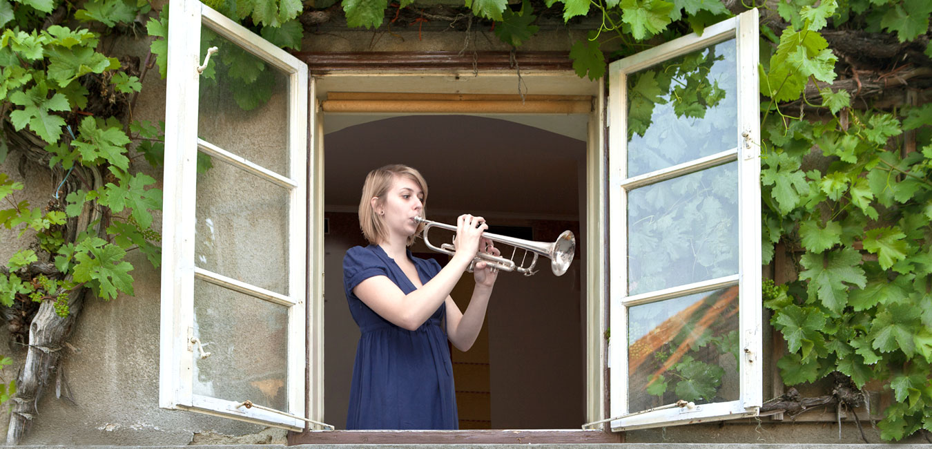 Frau spielt am offenem Fenster Trompete