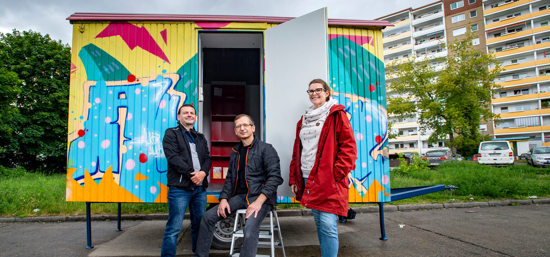 Drei Personen stehen vor einem bemalten Container.