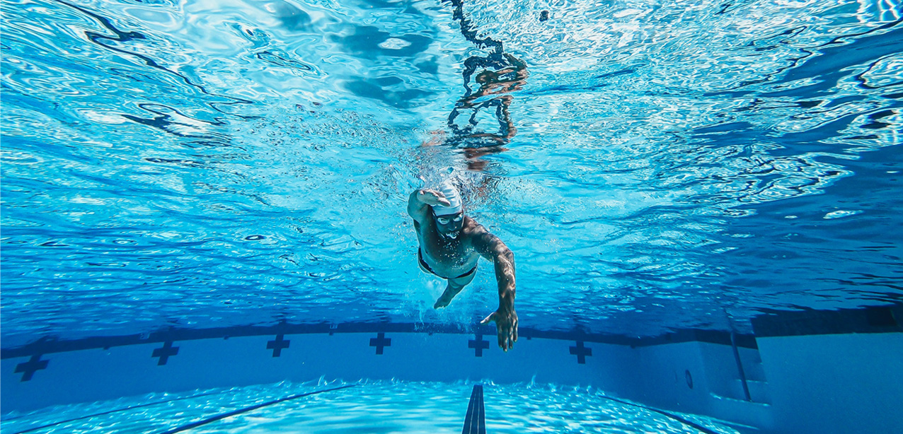 Unterwasseraufnahme eines männlichen Schwimmers in einem großen blauen Schwimmbecken.
