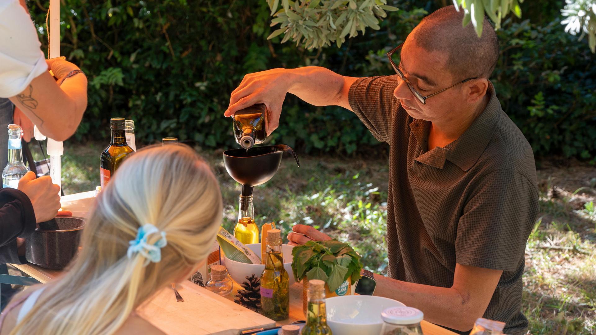 Ein Mann steht hinter einem Tisch und füllt eine Flüssigkeit über einem Trichter ab. Auf dem Tisch befinden sich verschiedene Gefäße stehen. Er