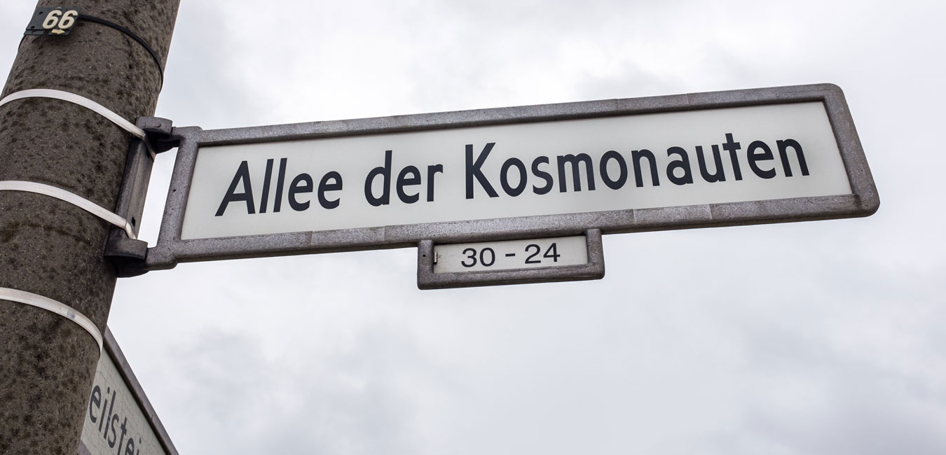 Strassenschild Alle der Kosmonauten: Schriften in schwarz vor dem weißen Hintergrund