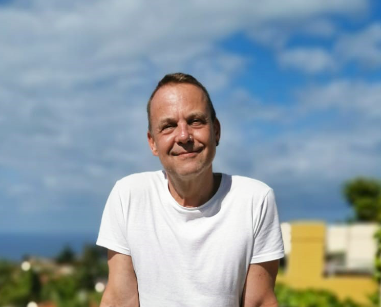 Stefan Lutz im weißen T-Shirt, eine verschwommenen Landschaft im Hintergrund.