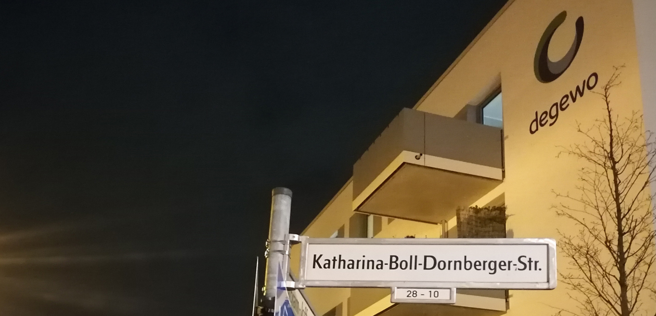 Das Straßenschild der Katharina-Boll-Dornberger-Straße. Das Logo von degewo ist auf einem Haus im Hintergrund zu erkennen.