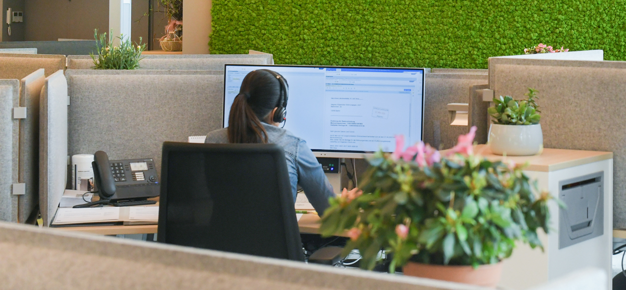 Frau sitzt im Büro mit Headset am Computer.