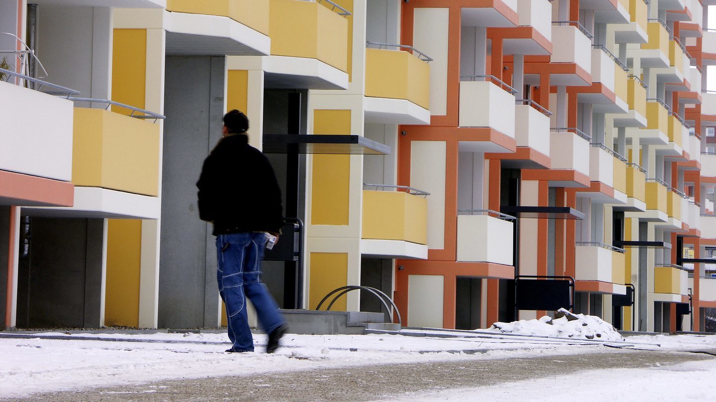 Wohnanlage im Winter mit gestreutem Fußgängerweg. Ein Mitarbeiter läuft den Weg ab.