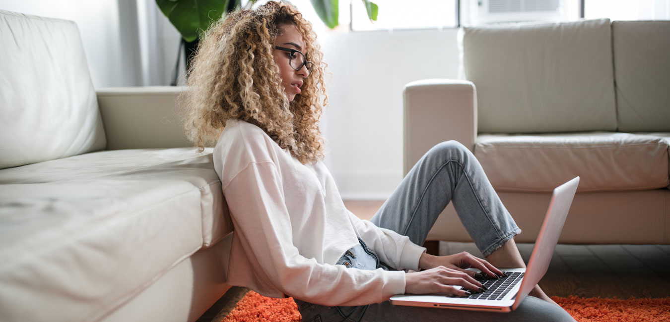 eine Frau, die sich an ein weißes Sofa lehnt und einen Laptop auf ihren Schoß legt.