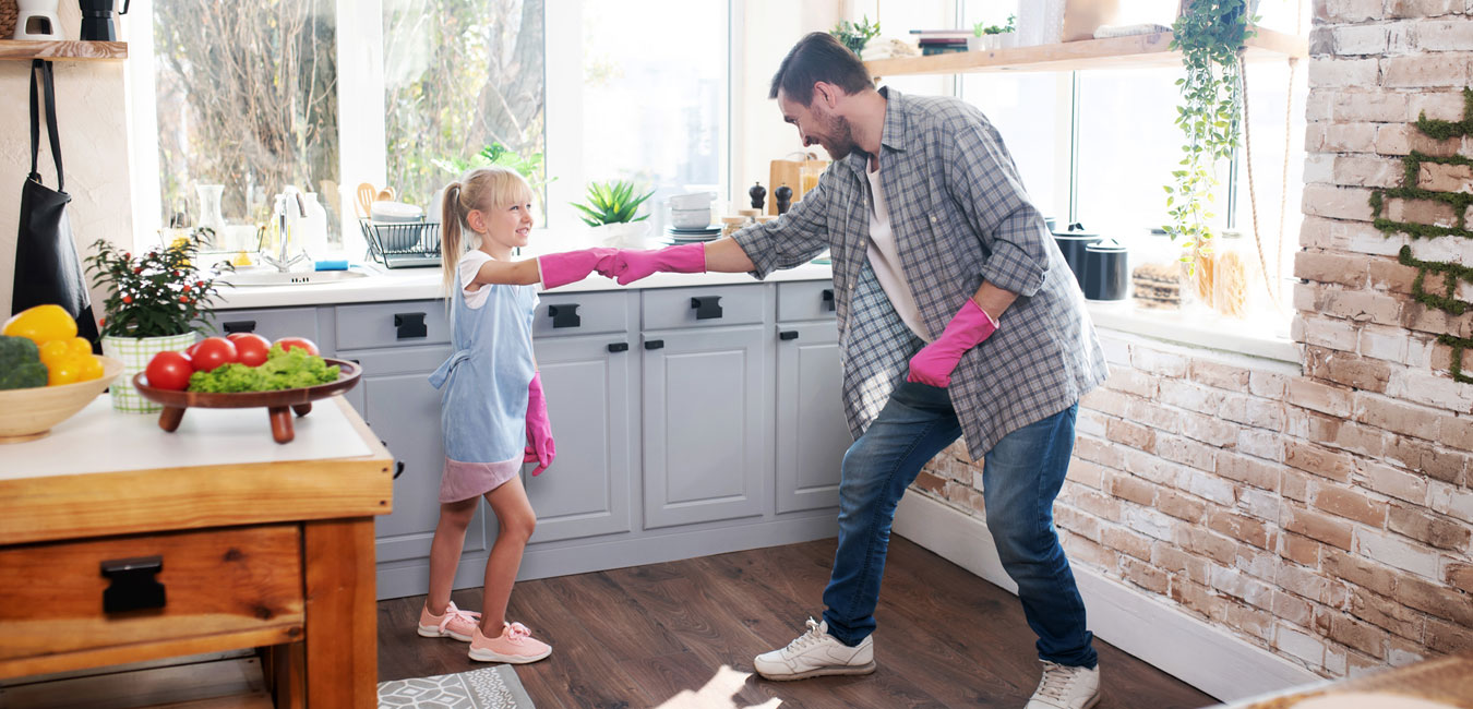 Das Foto zeigt Vater und Tochter mit pinken Gummihandschuhen in einer Küche. Beide lachen und machen einen Faustgruß.