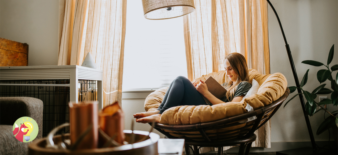 Eine Person sitzt zum Lesen in einem Sessel am Fenster. Das Zimmer ist mit warmen Farben dekoriert.