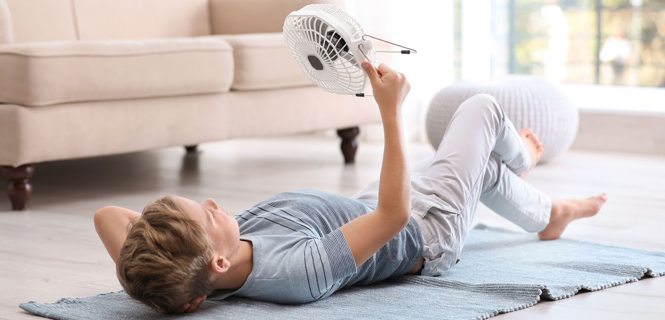 Junge liegt auf dem Boden und richtet einen Ventilator auf sich