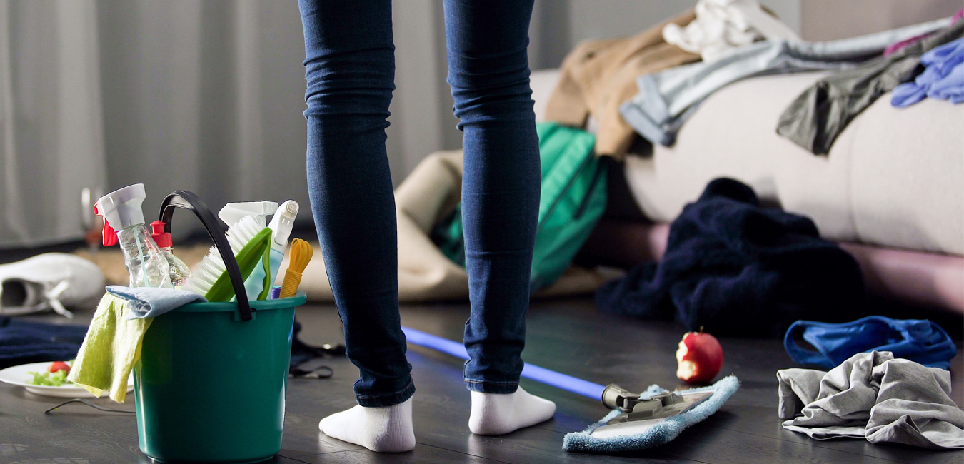 Foto aufgenommen von oberhalb des Knies einer Person nach unten. Unter dem Boden befinden sich Reinigungswerkzeuge. Viele Klamotten werden im Haus herumgeworfen.