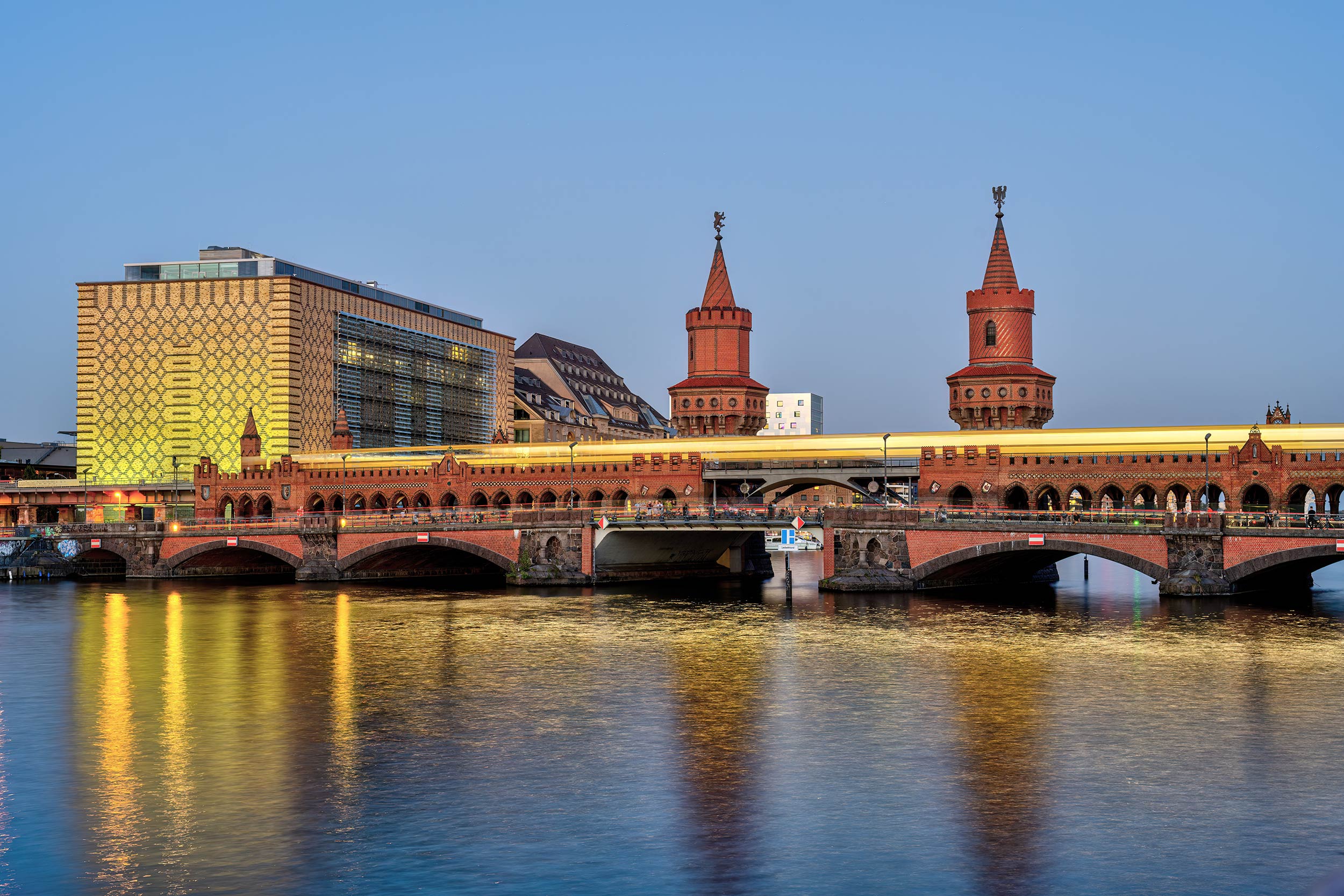 Blick vom Wasser auf eine beleuchtete Brücke aus rotem Stein.