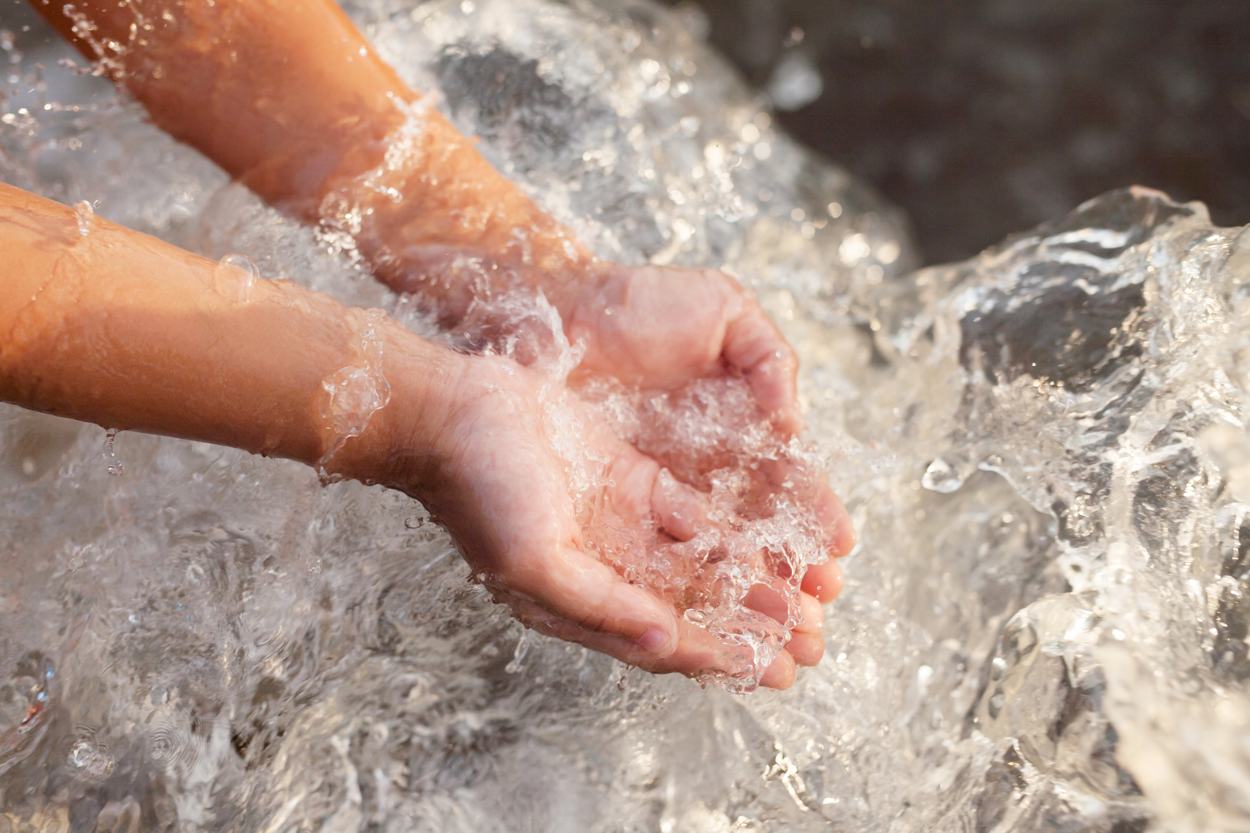 Zwei Kinderhände fangen literweise Wasser auf.