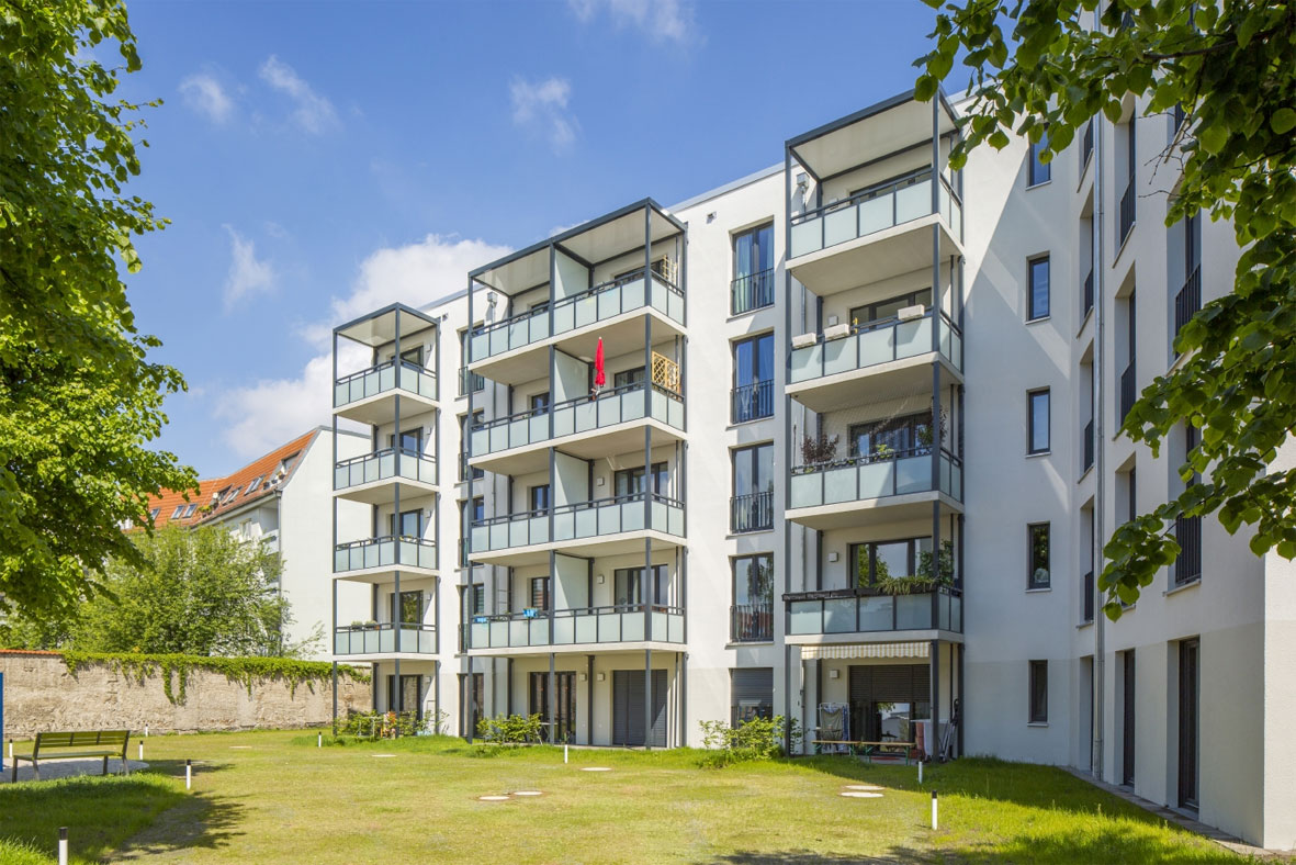 Blick auf ein mehrgeschossiges Wohnhaus mit Balkonen bei Sonnenschein.